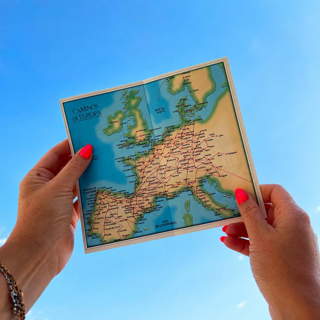 Manos sosteniendo un mapa en papel de las rutas del Camino de Santiago en Europa, con el cielo de fondo