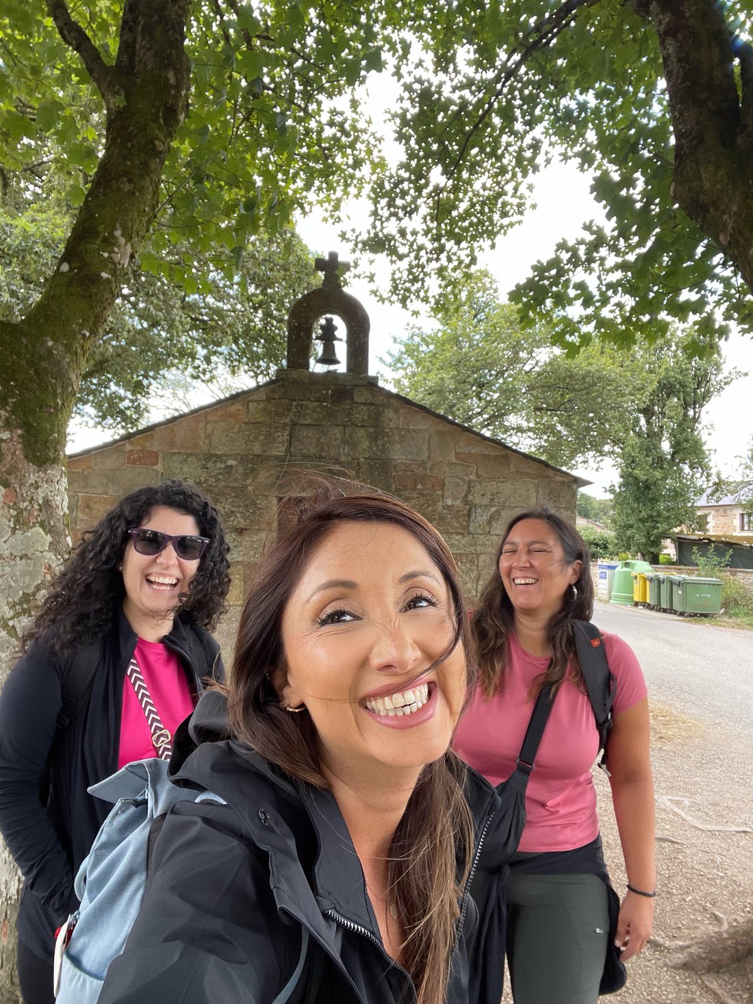 Less, Raquel y Fran sonriendo juntas frente a una capilla de piedra en el Camino de Santiago