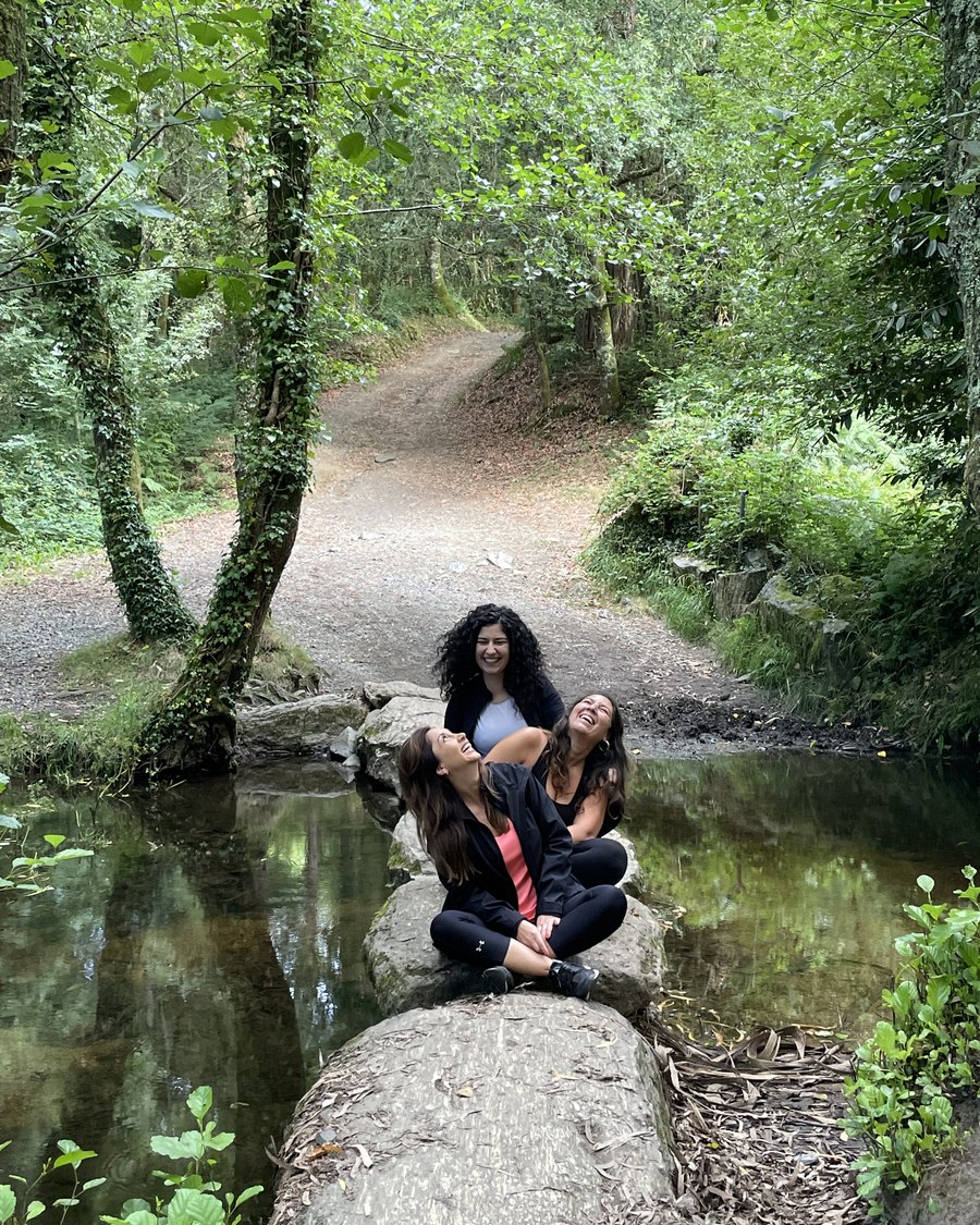 Less, Raquel y Fran riendo sentadas sobre unas rocas junto a un arroyo del Camino Francés