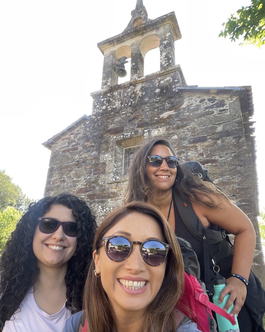 Less, Raquel y Fran sonriendo frente al campanario de piedra de una iglesia del Camino Francés